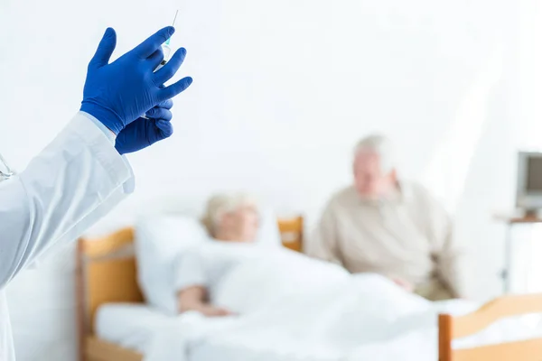 Частковий вигляд лікаря в латексних рукавичках, що тримає шприц, хворий пацієнт і старший чоловік в клініці — стокове фото
