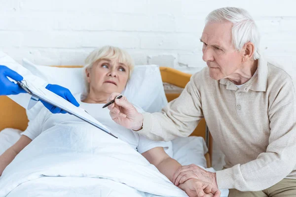 Partial view of doctor holding clipboard, sick patient and senior man in clinic — Stock Photo