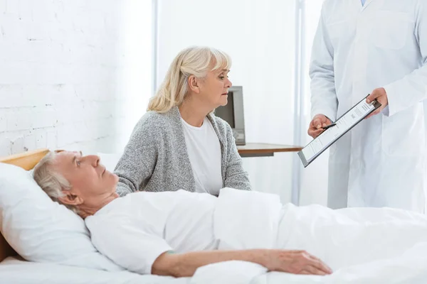 Partial view of doctor holding clipboard, sick patient and senior woman in clinic — Stock Photo