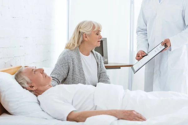 Vista parcial del médico portapapeles, paciente enferma y mujer mayor en la clínica - foto de stock