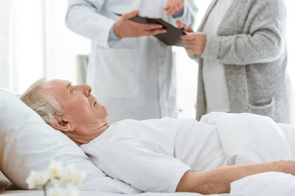 Vista parcial del médico portapapeles, paciente enferma y mujer mayor en la clínica - foto de stock