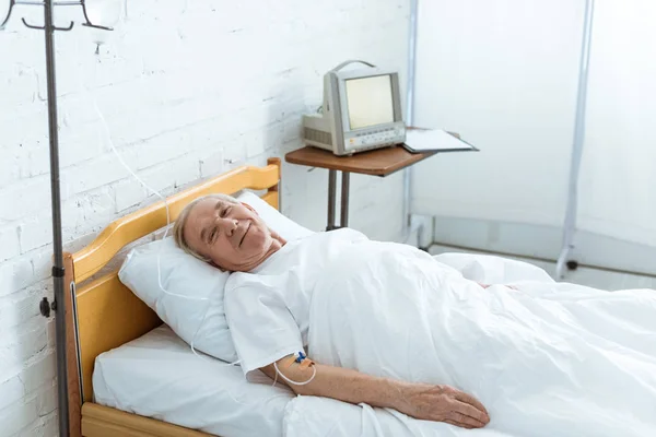 Sonriente anciano enfermo acostado en la cama en la clínica - foto de stock