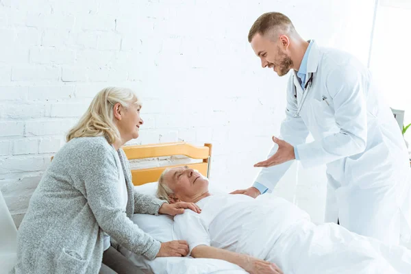 Médico sonriente y mujer mayor cerca de paciente enfermo en la clínica - foto de stock