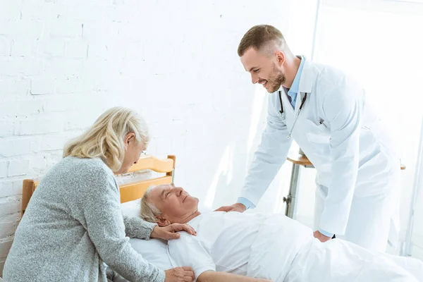 Médico sonriente y mujer mayor cerca de paciente enfermo en la clínica - foto de stock