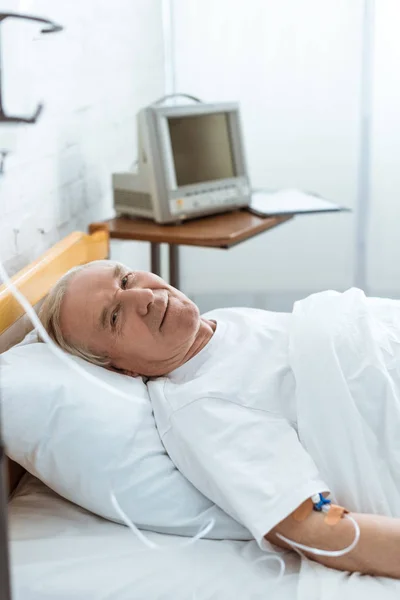 Krank lächelnder Senior liegt im Krankenhaus auf Bett — Stockfoto