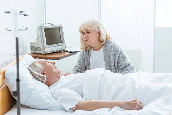 Worried senior woman looking at ill husbend in hospital — Stock Photo