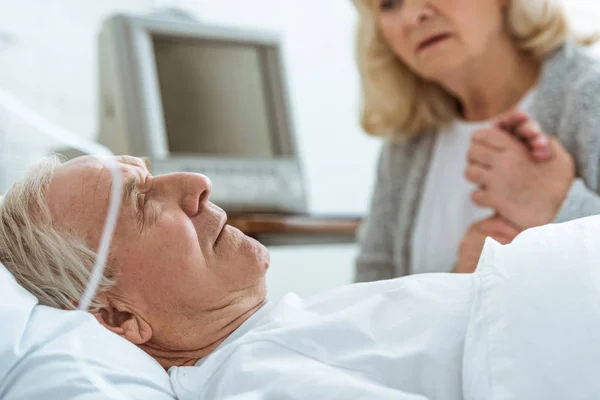 Vue partielle d'une femme âgée inquiète assise près d'un mari malade et tenant sa main à l'hôpital — Photo de stock