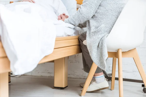 Vista recortada de la mujer mayor cogida de la mano con marido enfermo en el hospital - foto de stock