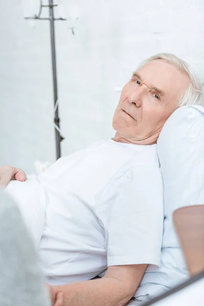 Kranker Senior liegt auf Bett und blickt in Klinik in Kamera — Stockfoto