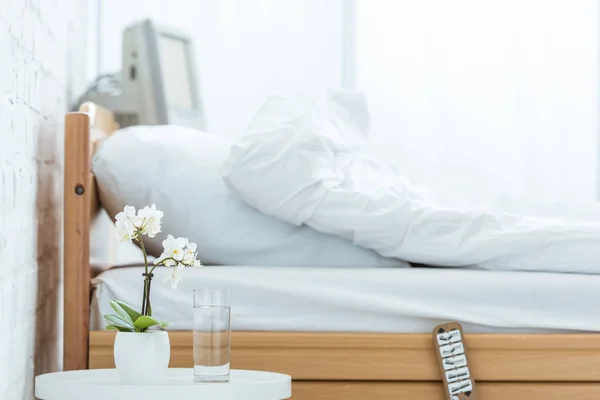 Cama vazia, orquídeas e copo de água na enfermaria do hospital — Fotografia de Stock