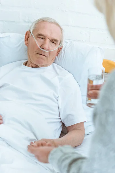 Vista recortada de la mujer mayor dando vaso de agua al marido enfermo en el hospital - foto de stock