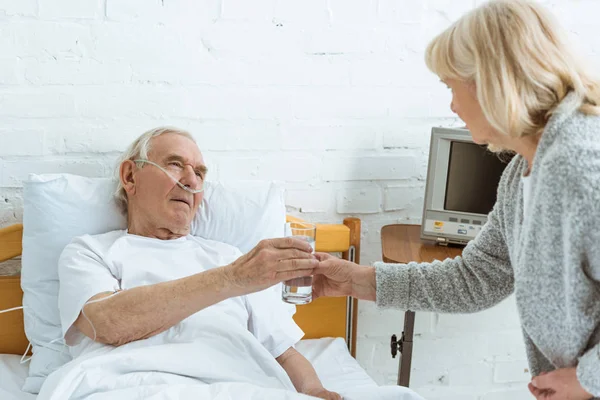 Mujer mayor dando vaso de agua a marido enfermo en el hospital — Stock Photo