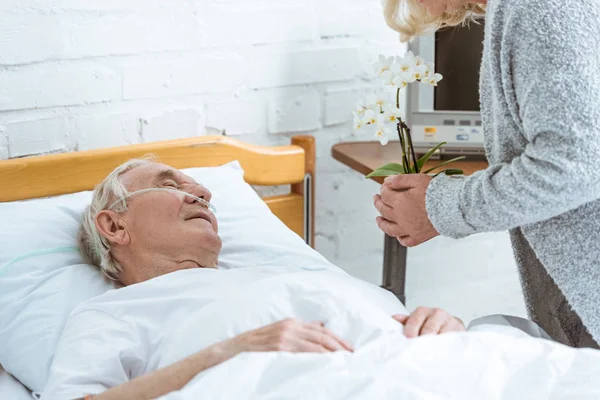 Vista ritagliata di donna anziana con orchidee e paziente malato in ospedale — Foto stock