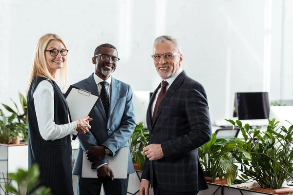 Selective focus of cheerful businessmen and businesswoman standing in office — Stock Photo