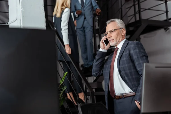 Selective focus of businessman talking on smartphone near multicultural partners — Stock Photo