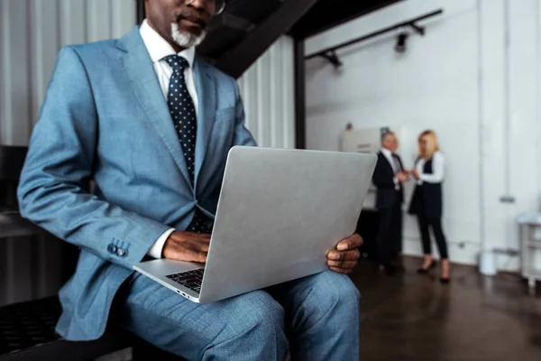 Cropped view of african american businessman using laptop near coworkers — Stock Photo