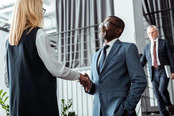 Low angle view of blonde businesswoman shaking hands with african american businessman — Stock Photo