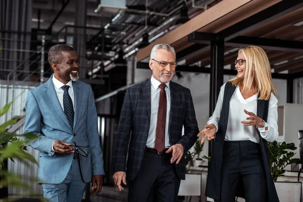 Selektiver Fokus einer glücklichen Geschäftsfrau, die gestikuliert, während sie mit multikulturellen Partnern im Büro lächelt — Stockfoto