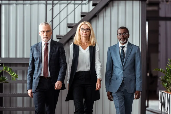 Attractive blonde businesswoman walking with handsome multicultural partners in office — Stock Photo