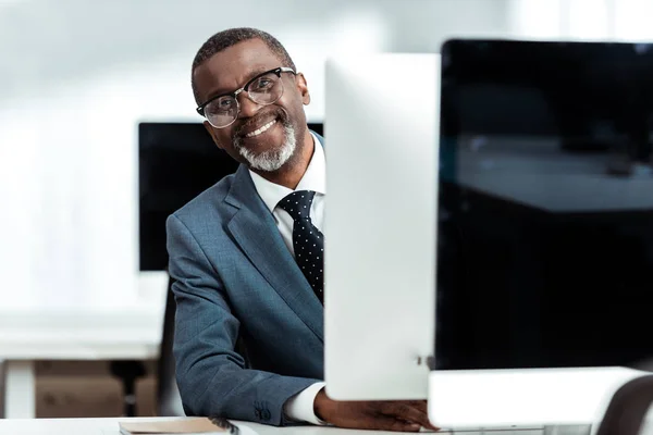 Щасливий афроамериканський бізнесмен в окулярах посміхається в офісі — стокове фото