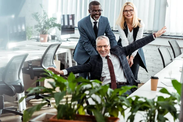 Selective focus of happy businessman with outstretched hands near cheerful multicultural coworkers — Stock Photo