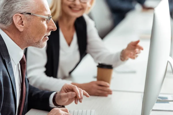 Selektiver Fokus des Geschäftsmannes mit Brille, der in der Nähe einer blonden Frau auf den Computermonitor blickt — Stockfoto