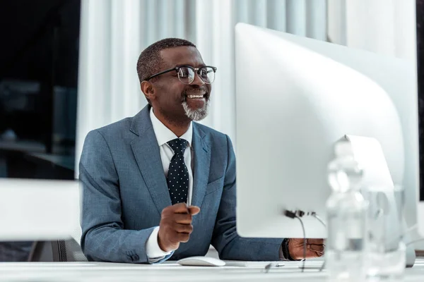 Vista basso angolo di felice uomo d'affari africano americano guardando monitor del computer in ufficio — Foto stock