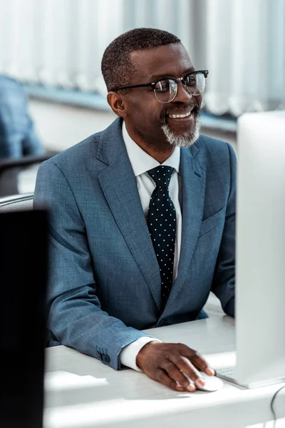 Избирательный фокус счастливого африканского американского бизнесмена, смотрящего на монитор компьютера в офисе — стоковое фото