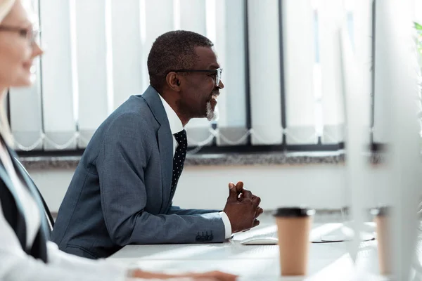 Enfoque selectivo de hombre afroamericano feliz mirando monitor de computadora cerca de mujer rubia - foto de stock