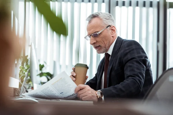 Selective focus of handsome businessman reading newspaper while holding disposable cup — Stock Photo