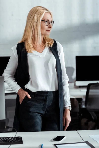 Привлекательная блондинка стоящая с рукой в кармане в офисе — стоковое фото