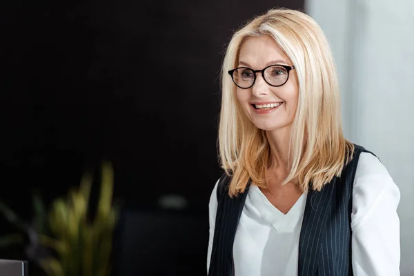 Glückliche blonde und attraktive Geschäftsfrau mit Brille, die im Büro lächelt — Stockfoto