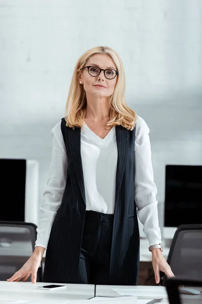 Attraktive blonde Geschäftsfrau mit Brille blickt im Büro in die Kamera — Stockfoto