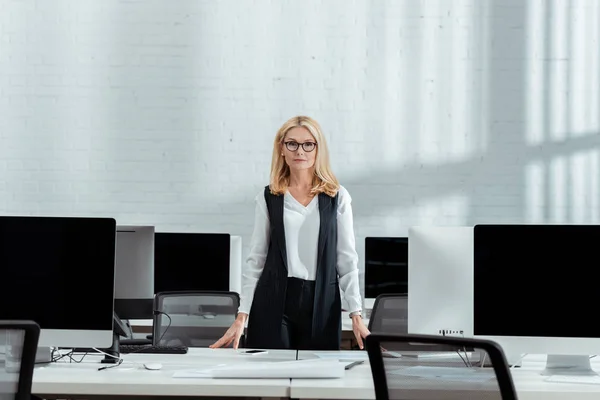 Приваблива блондинка-бізнесмен стоїть біля комп'ютерних моніторів з порожніми екранами в офісі — стокове фото