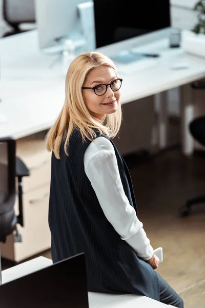 Vista aerea di attraente donna d'affari bionda in occhiali sorridente in ufficio — Foto stock