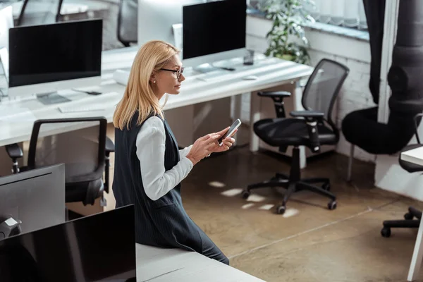 Vista aérea de la mujer de negocios reflexiva en gafas usando teléfono inteligente - foto de stock