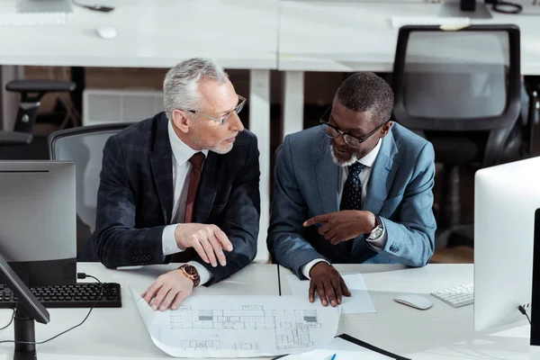 Vista aérea de hombres de negocios multiculturales hablando cerca de planos en la oficina — Stock Photo