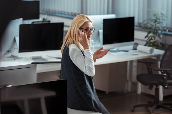 Attrayant femme d'affaires en lunettes geste tout en parlant sur smartphone — Photo de stock