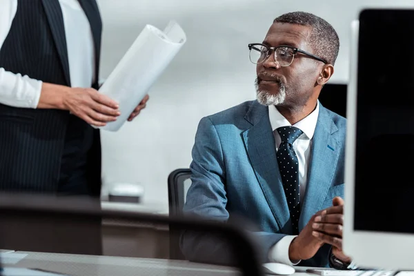 Vista recortada de la mujer de negocios sosteniendo planos cerca de hombre de negocios afroamericano - foto de stock