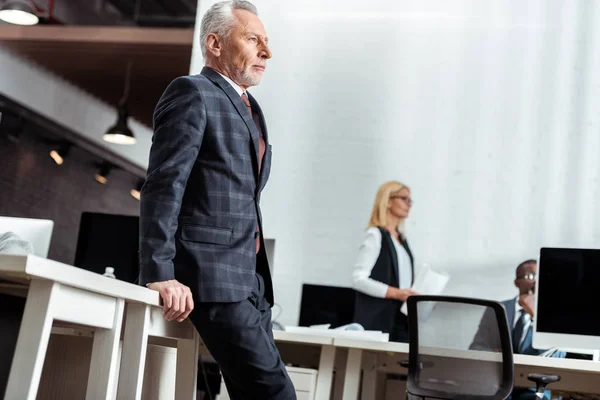 Vista de bajo ángulo del hombre de negocios de pie cerca de colegas multiculturales en la oficina - foto de stock