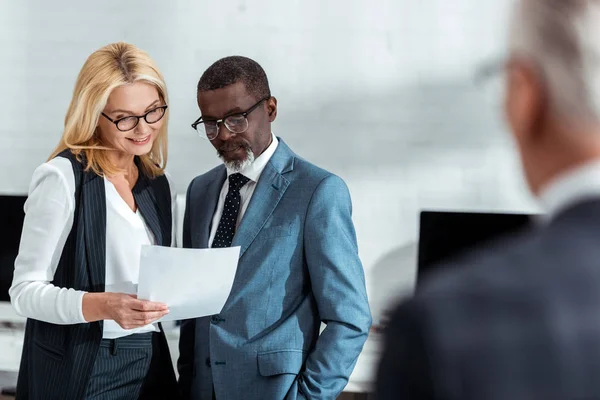 Selective focus of cheerful businesswoman and african american businessman looking at document near partner — Stock Photo