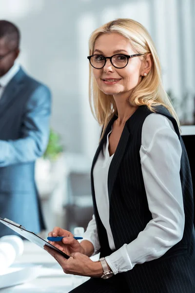 Selective focus of cheerful blonde woman smiling near african american businessman — Stock Photo