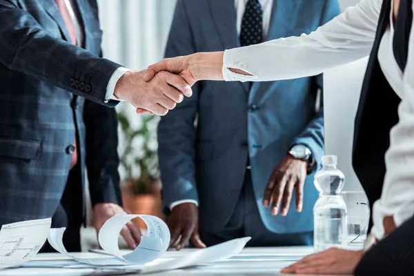 Vista recortada de hombre de negocios y mujer de negocios estrechando la mano cerca de socio afroamericano - foto de stock