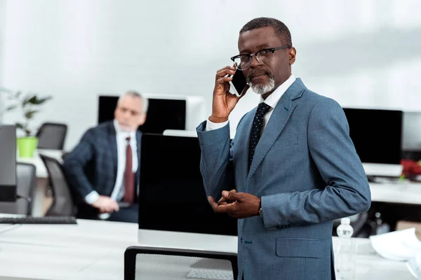 Enfoque selectivo de hombre de negocios afroamericano hablando en el teléfono inteligente socio cercano - foto de stock