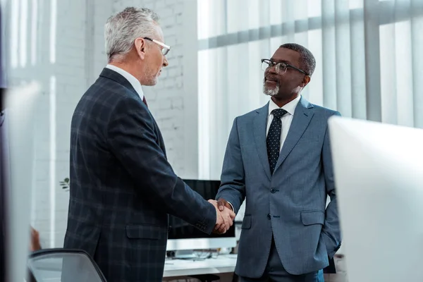 Low angle view of multicultural businessmen shaking hands in office — Stock Photo