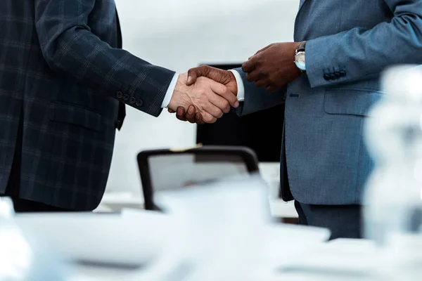 Vista recortada del hombre de negocios afroamericano estrechando la mano con el socio en la oficina - foto de stock