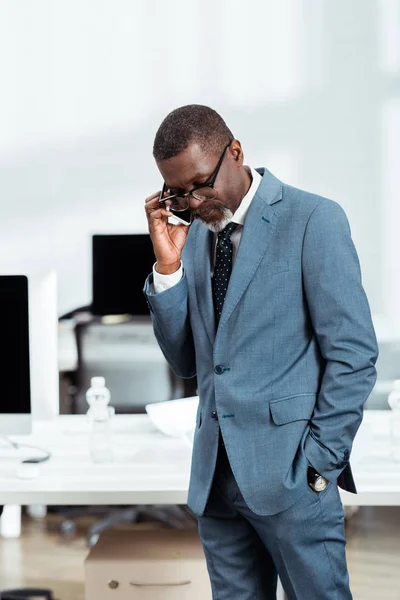 Bel homme d'affaires afro-américain en lunettes parlant sur smartphone au bureau — Photo de stock