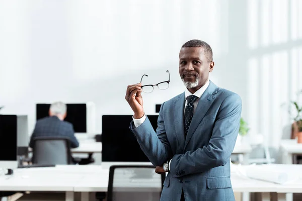 Enfoque selectivo del hombre de negocios afroamericano sosteniendo gafas en el cargo - foto de stock