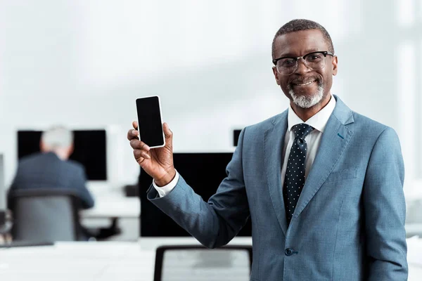 Selektiver Fokus glücklicher afrikanisch-amerikanischer Geschäftsmann mit Smartphone mit leerem Bildschirm im Büro — Stockfoto