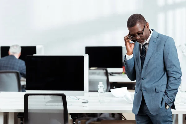 Foco seletivo de belo empresário afro-americano em terno falando no smartphone no escritório — Fotografia de Stock